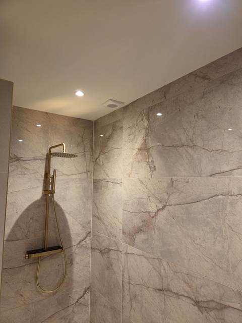 Badkamer in marmerlook met gouden regendouche en strak plafond